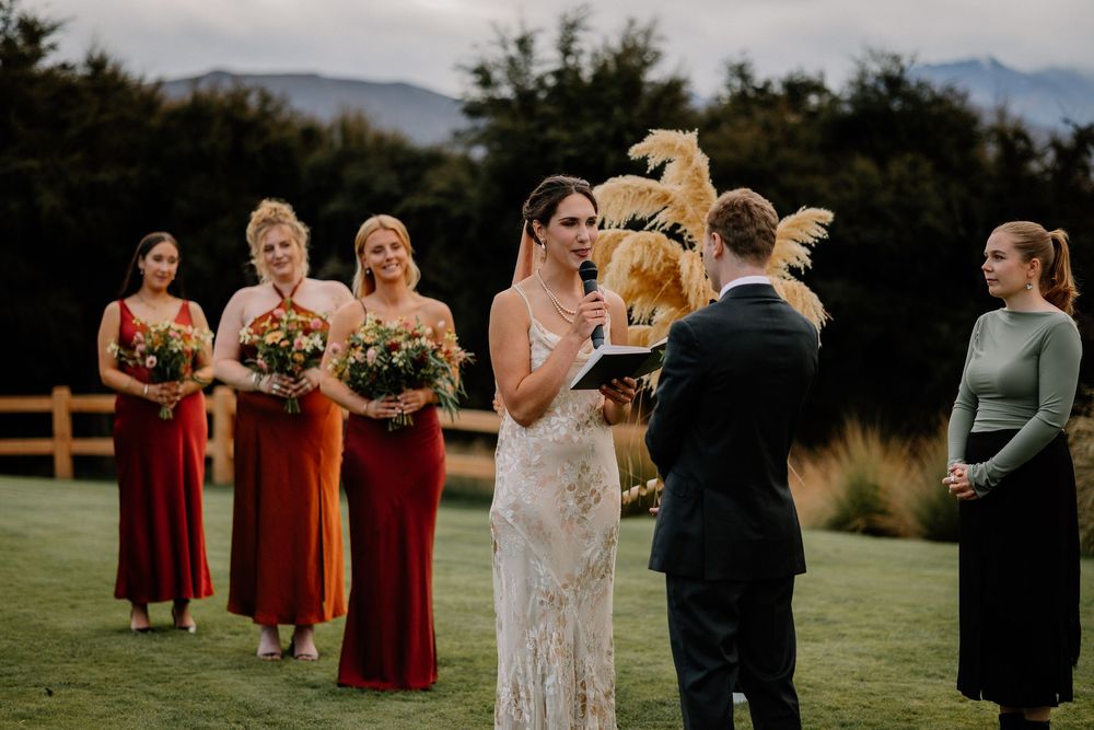 An outdoor wedding ceremony features rustic decor with burgundy bridesmaid dresses against a scenic mountain backdrop.