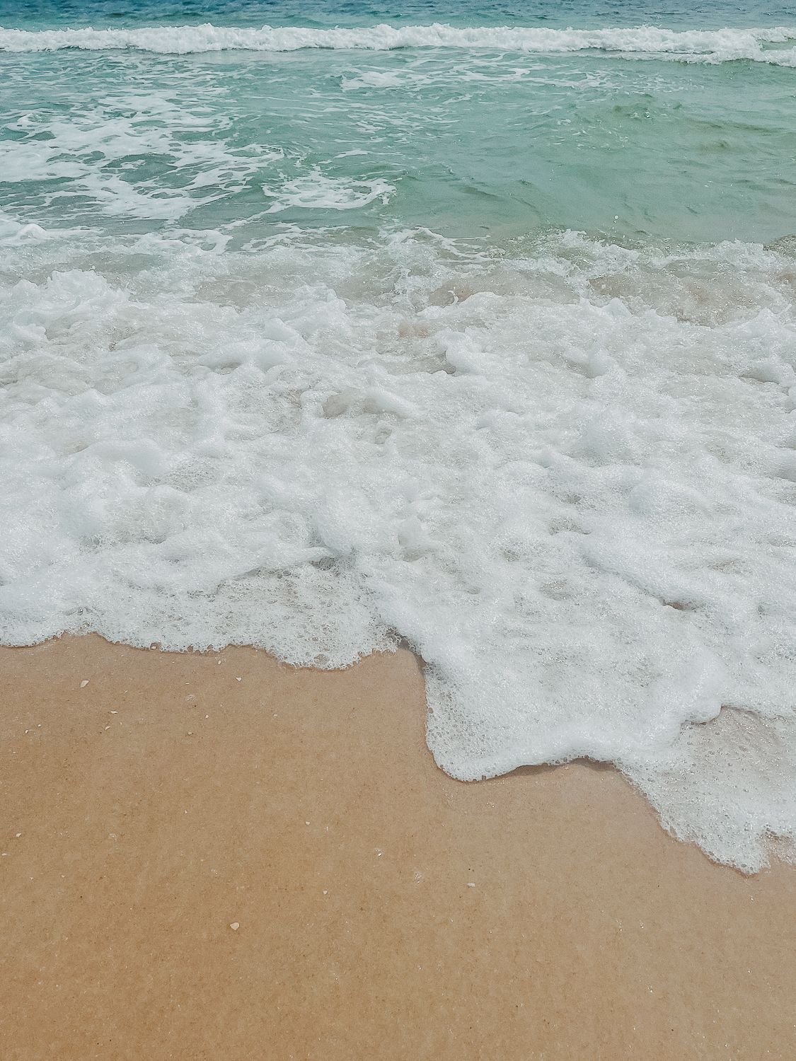 Turquoise ocean waves crash onto a pristine sandy beach creating white foam patterns along the shoreline.