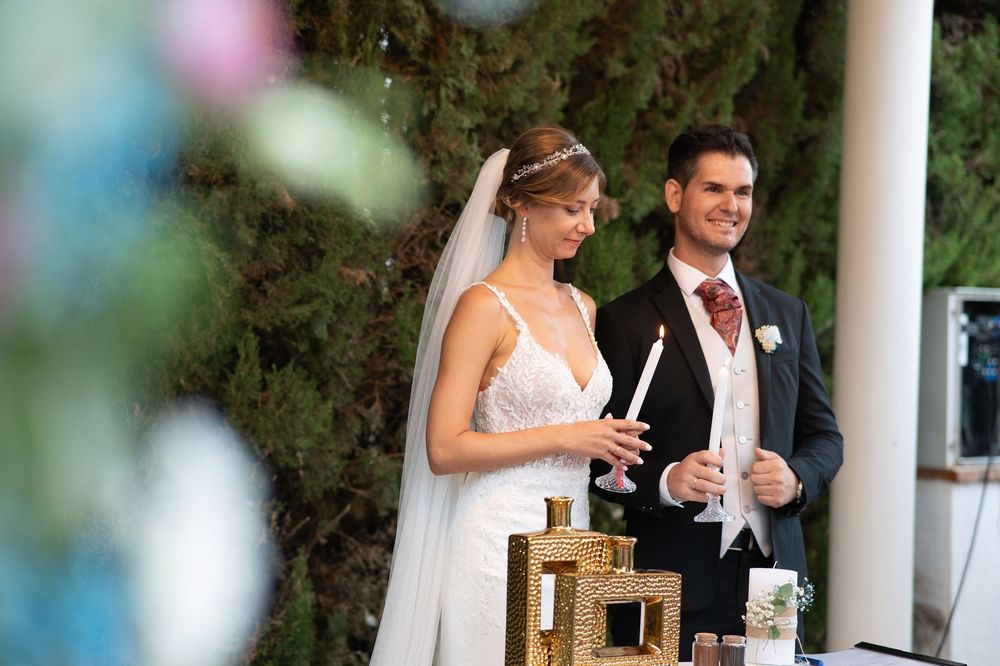 A couple raises champagne glasses during a wedding toast at an elegant outdoor ceremony in front of lush greenery.