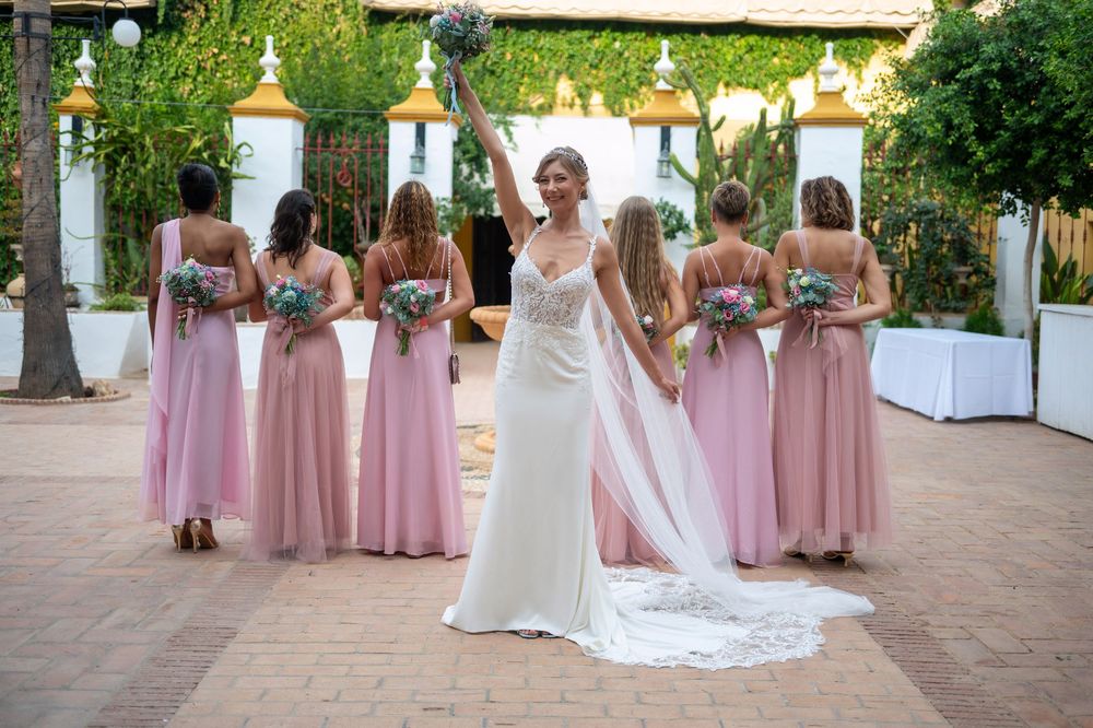 A wedding party with bridesmaids in pink dresses and a bride in white gown posing together on a terrace.
