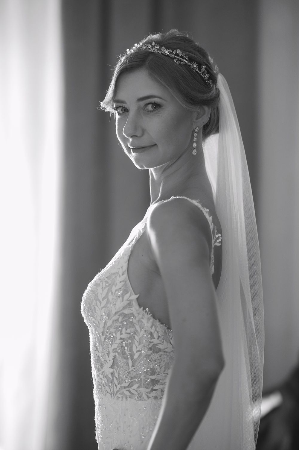 Elegant bride in black and white wearing a lace wedding dress, veil and delicate headpiece glances over her shoulder.