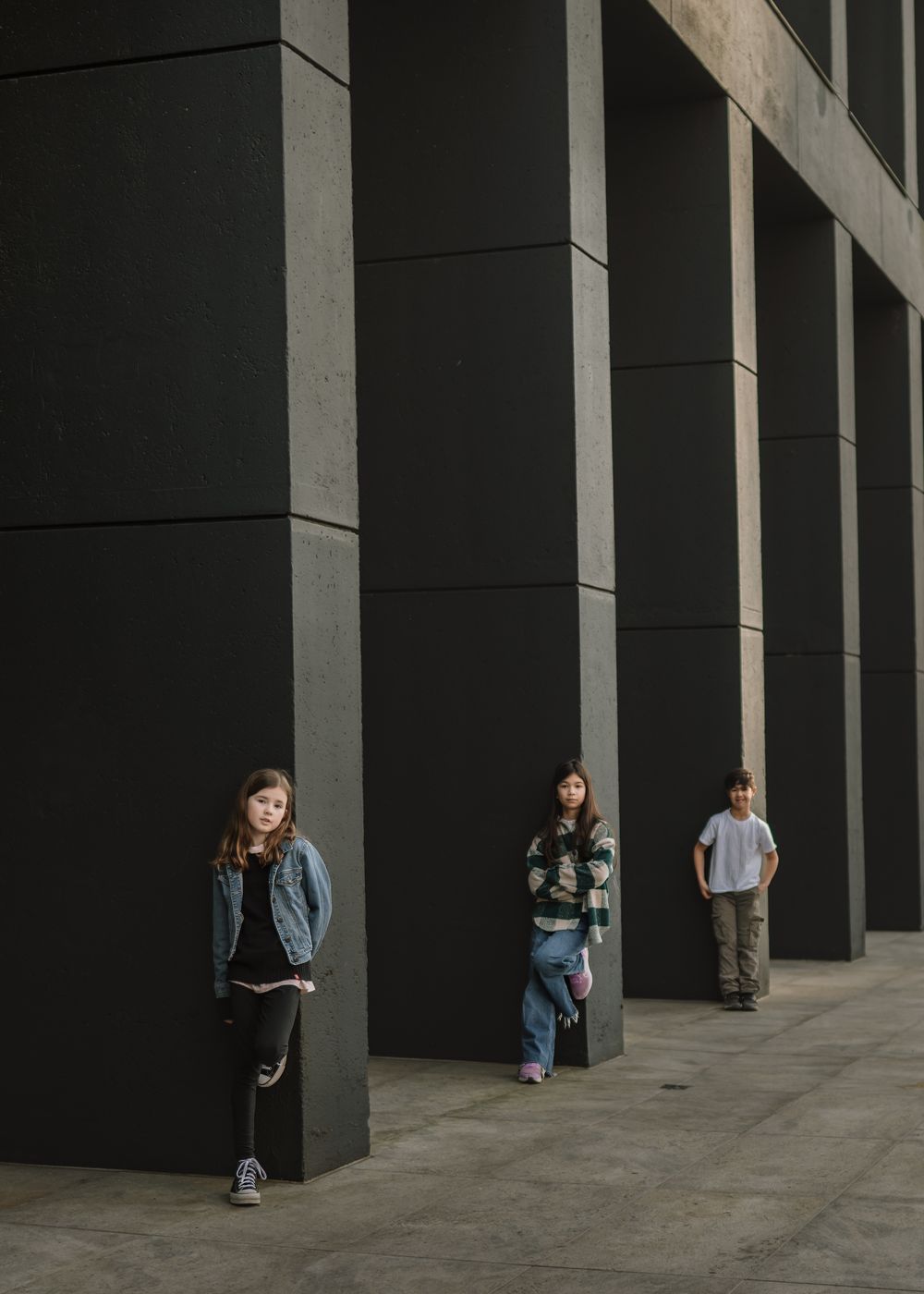 Three people posing against dark pillars in an urban setting with dramatic shadows and lighting.