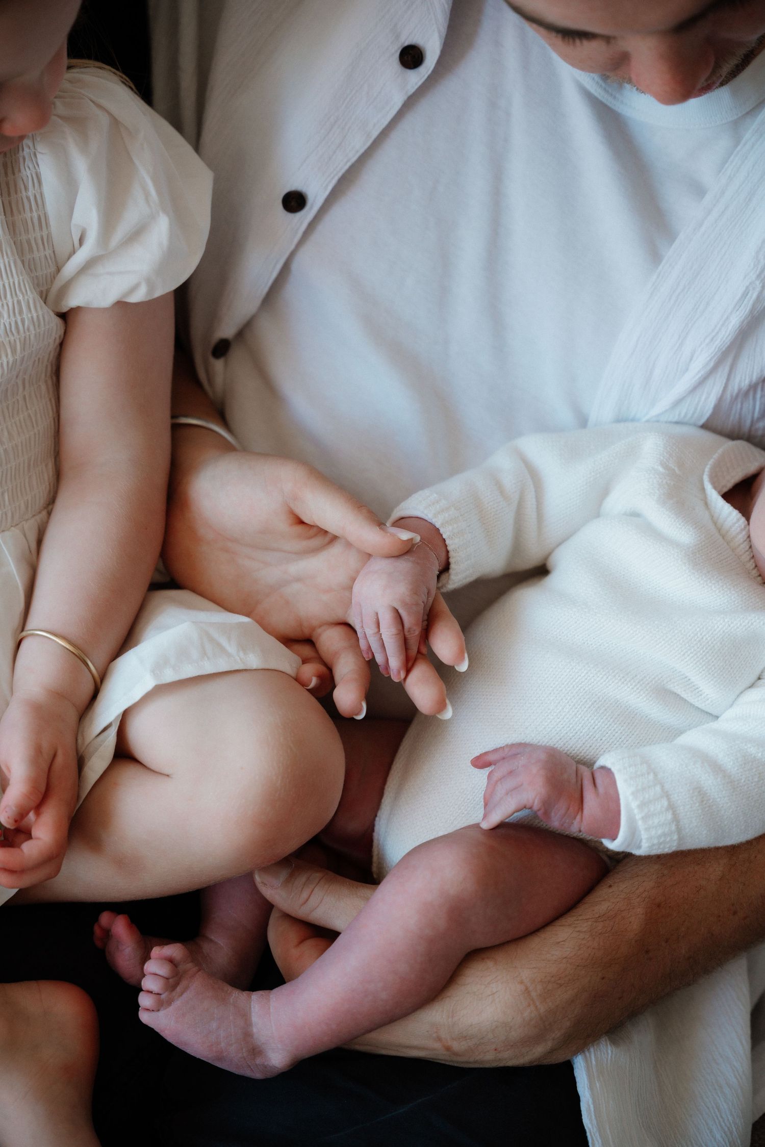 Close-up view of hands holding a baby's tiny feet and legs against white fabric.