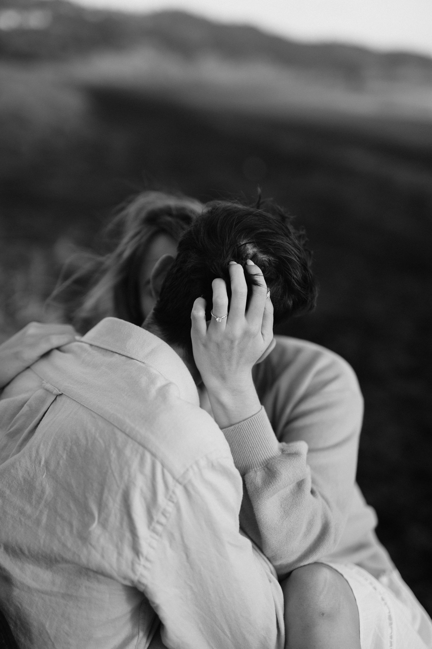 Black and white artistic portrait of person with windswept hair against mountain backdrop.