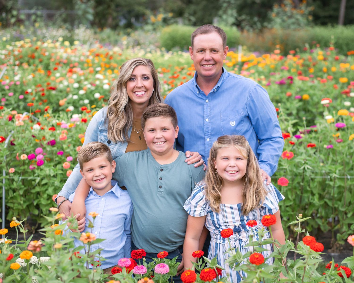 A family poses together in a vibrant garden filled with colorful orange, pink and red wildflowers in bloom.