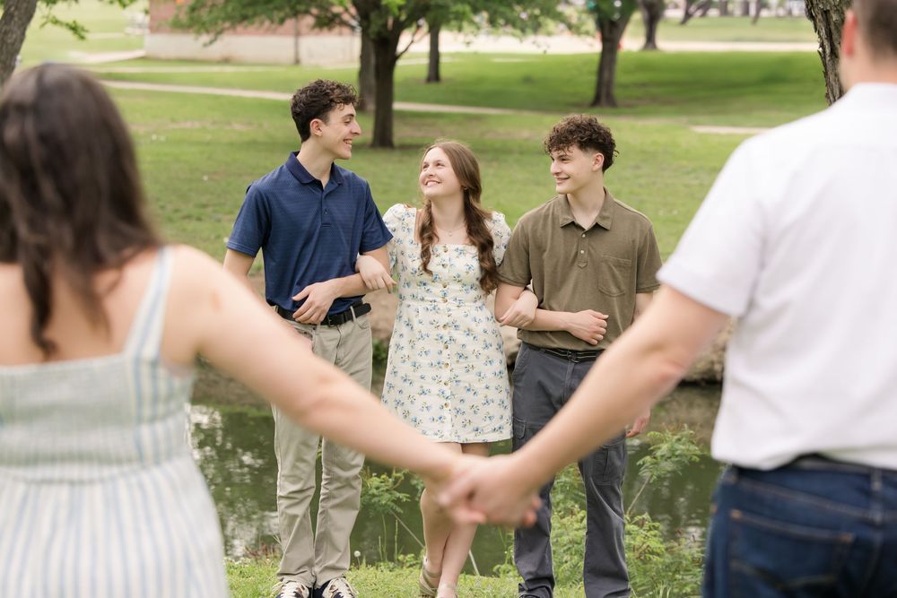 Group of friends laughing and talking together outdoors on a sunny day in a park setting.