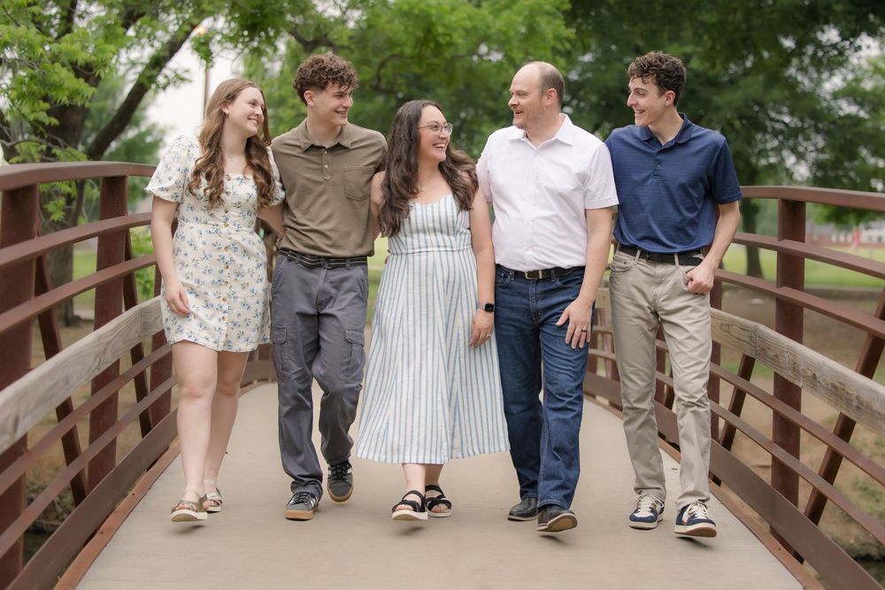 A group of young people walking together and smiling on a wooden bridge surrounded by greenery.