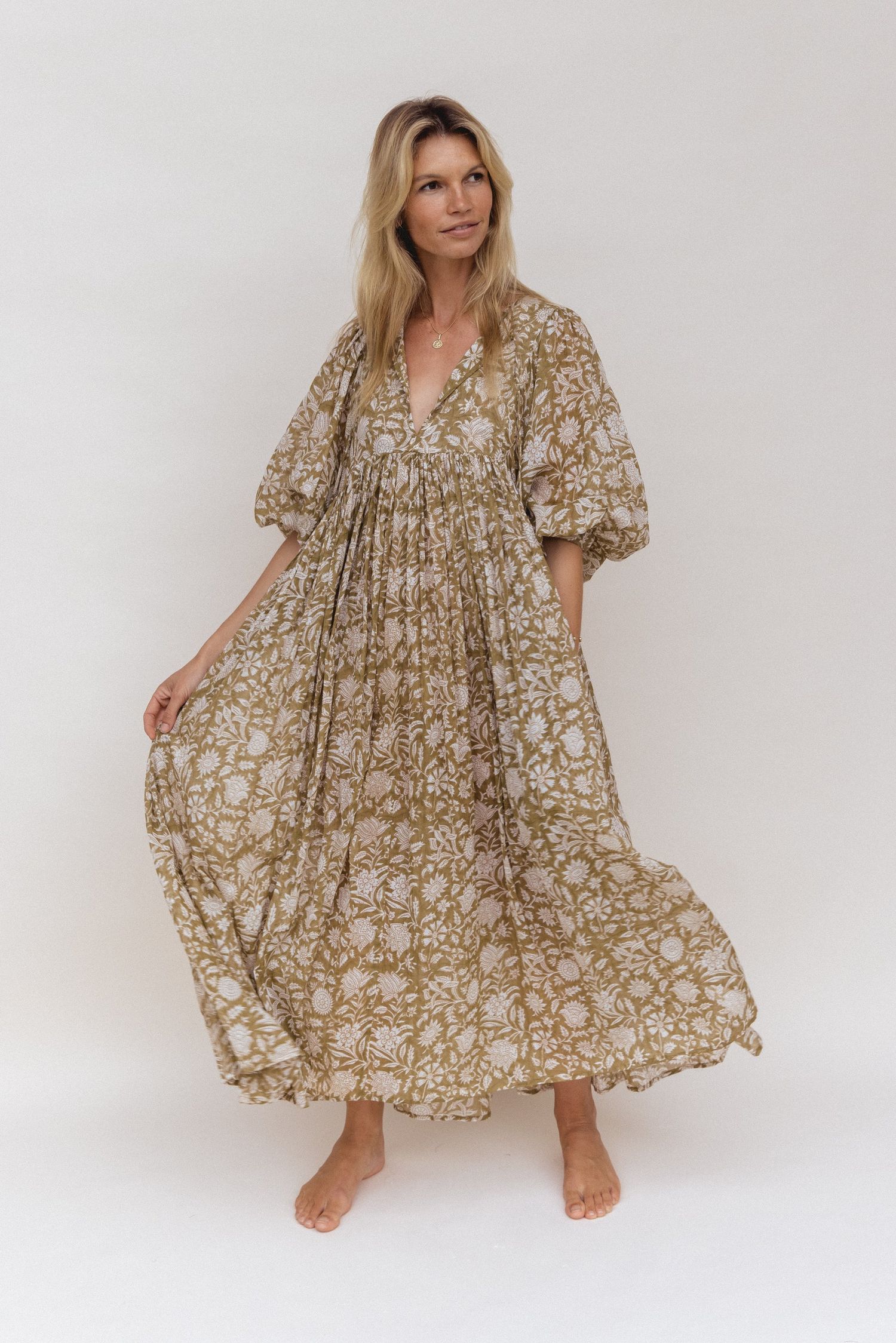 Flowy maxi dress in brown and white floral print with balloon sleeves and empire waist shown on barefoot model against white backdrop.