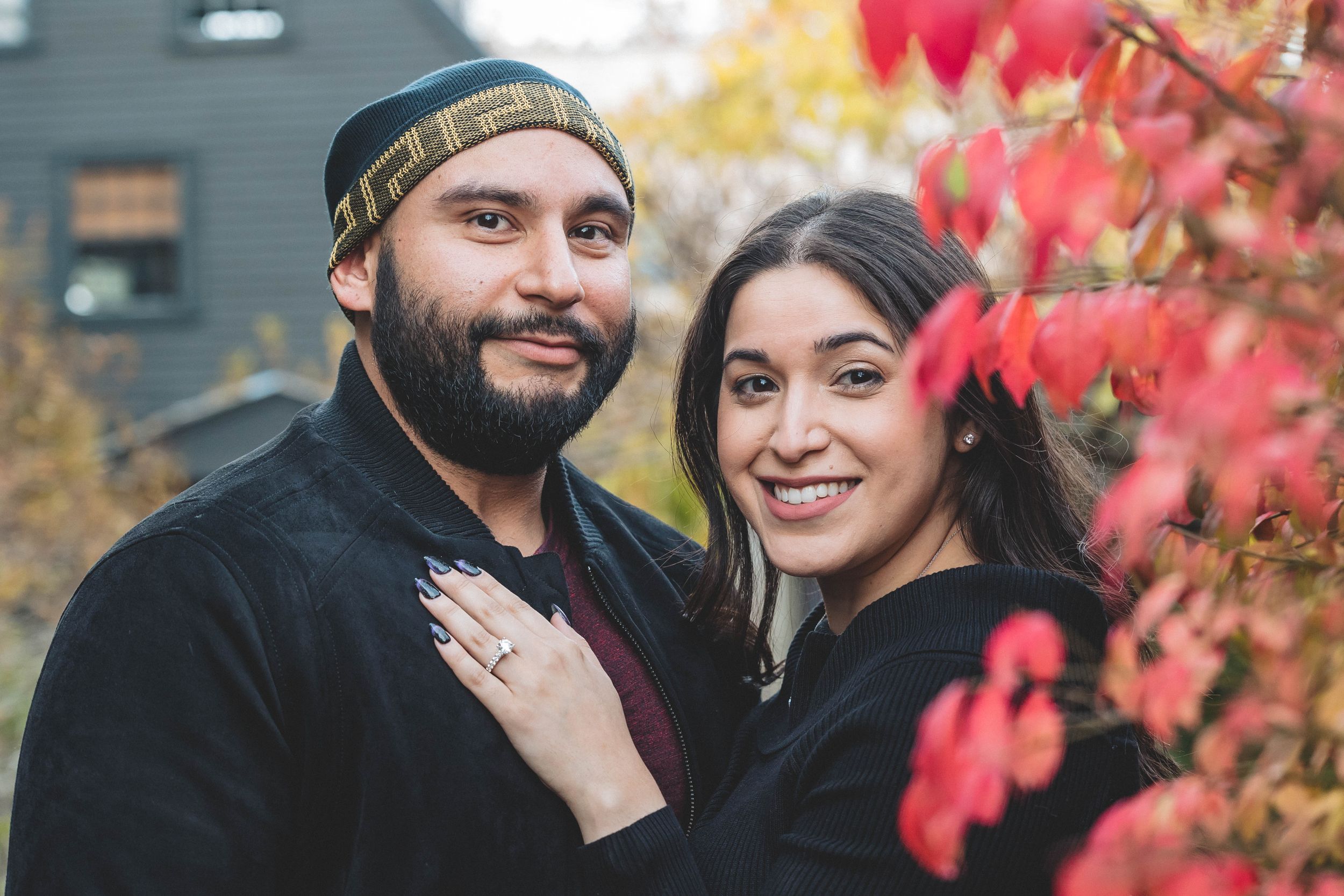 A couple poses together against vibrant red autumn foliage for their engagement photos.