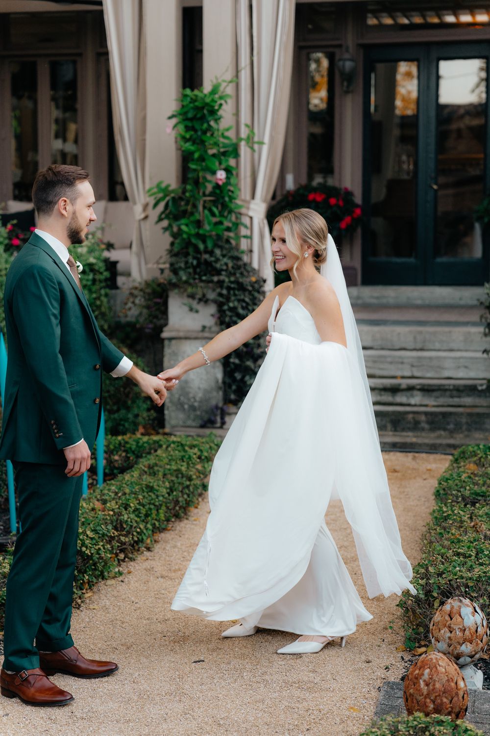 A couple shares a romantic first look moment in a garden setting, with the bride in white and groom in emerald green attire.