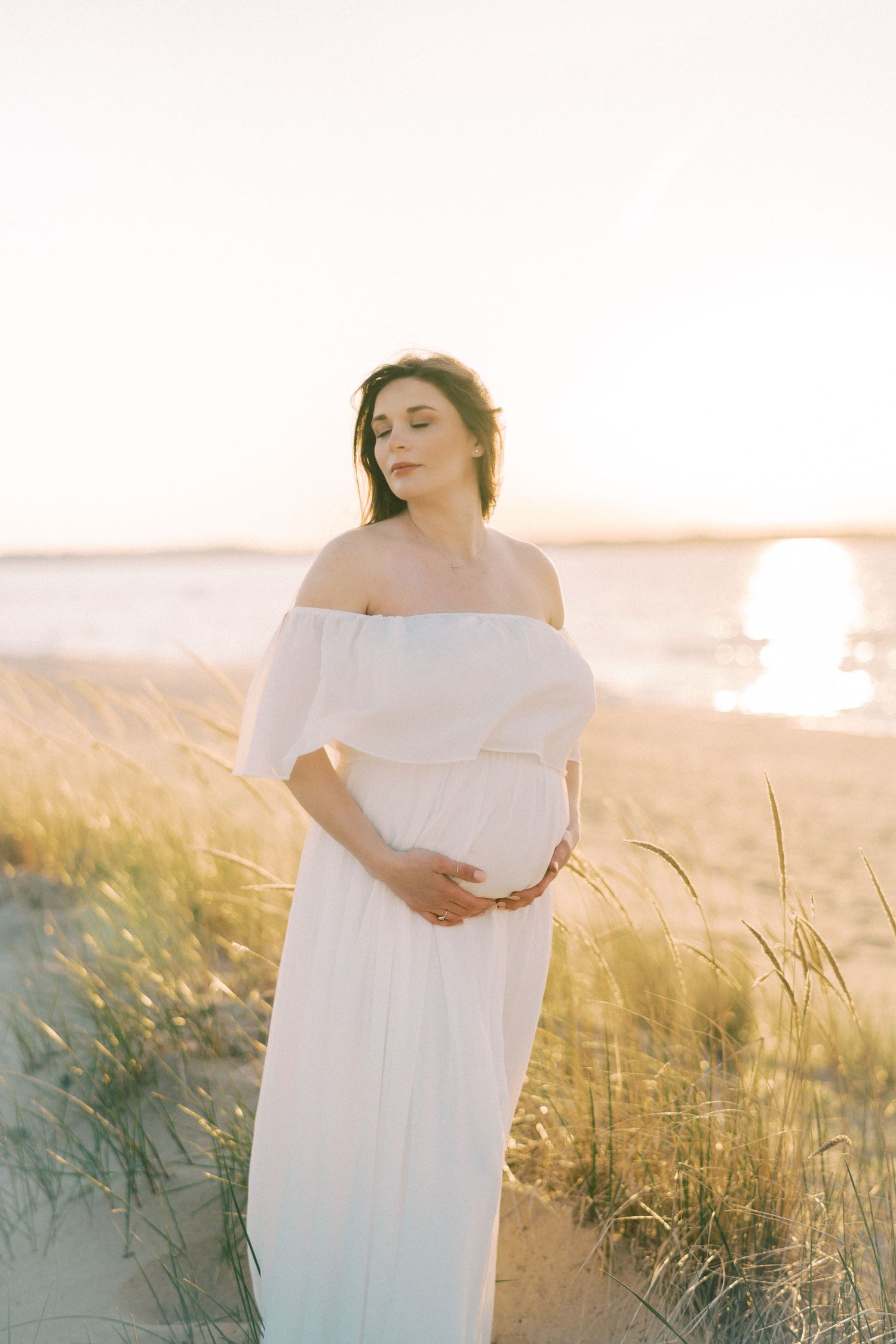 A maternity portrait in a fall field with a woman wearing a brown hat and knit sweater.
