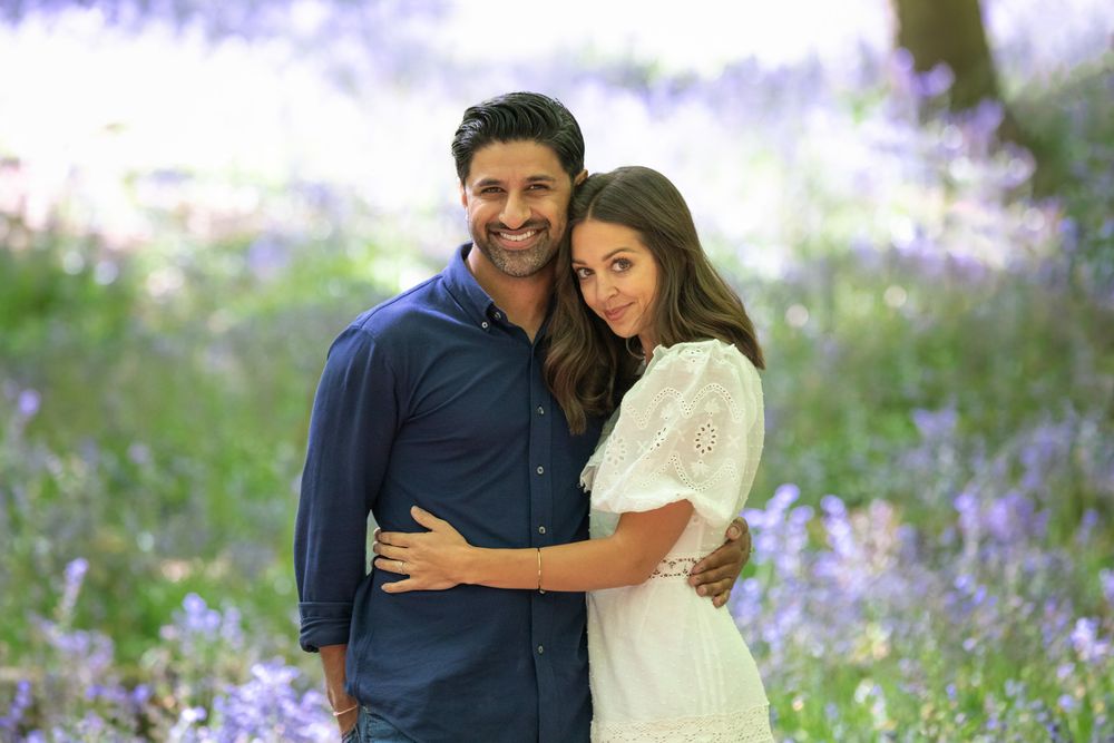 A romantic couple embraces in a meadow filled with blooming purple wildflowers on a bright summer day.