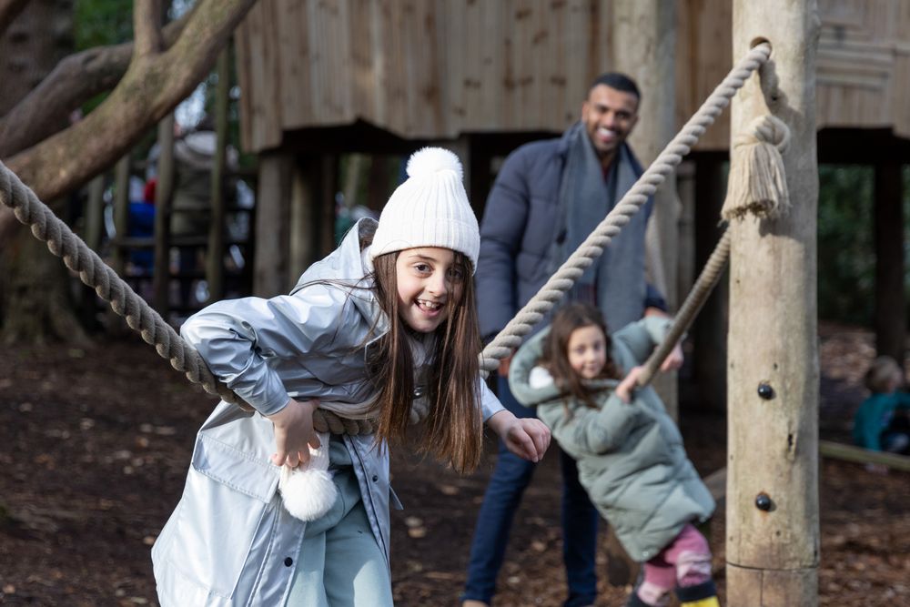 People enjoying outdoor activities at a playground with climbing ropes and wooden structures.