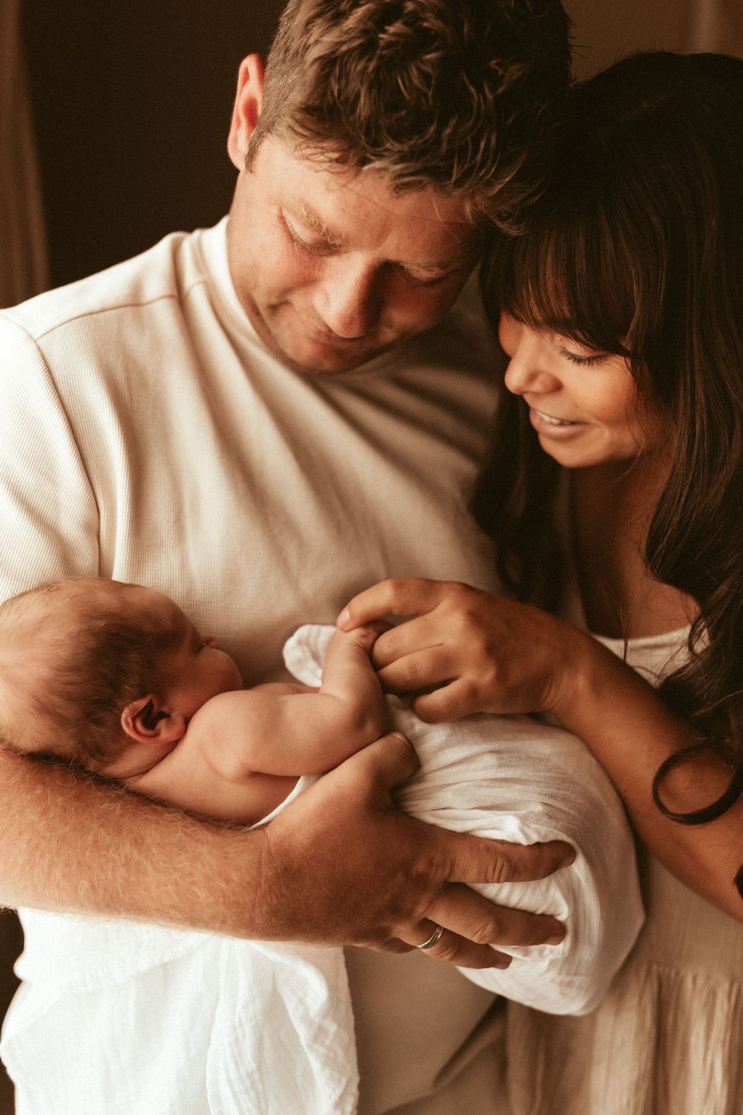 A tender moment as parents cradle their newborn baby in a warm-toned intimate portrait. Javea newborn photographer