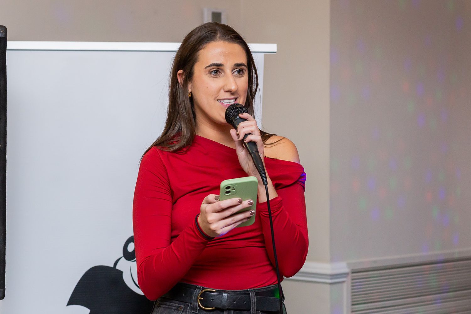 Speaker in red sweater holds microphone and phone during presentation.