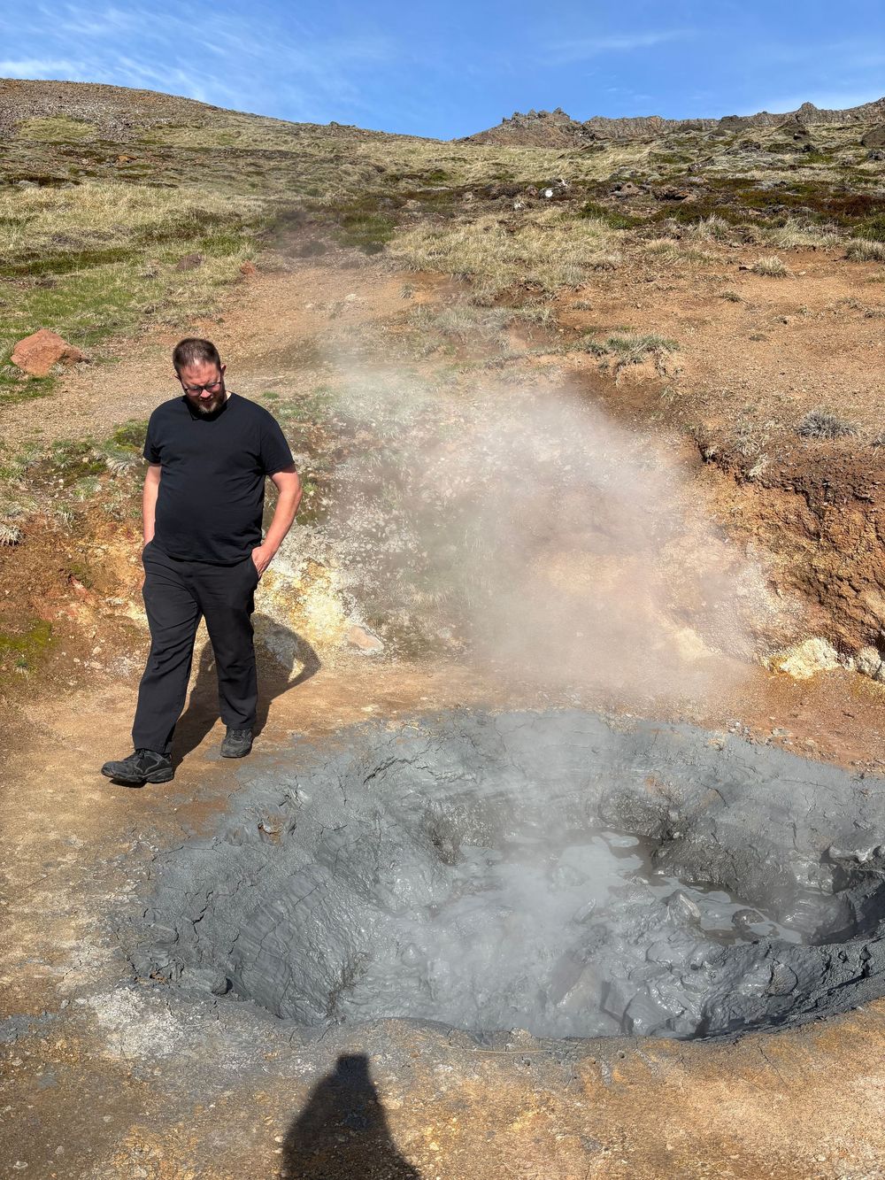 Steam rises from a geothermal hot spot in rocky terrain under blue skies in Iceland.