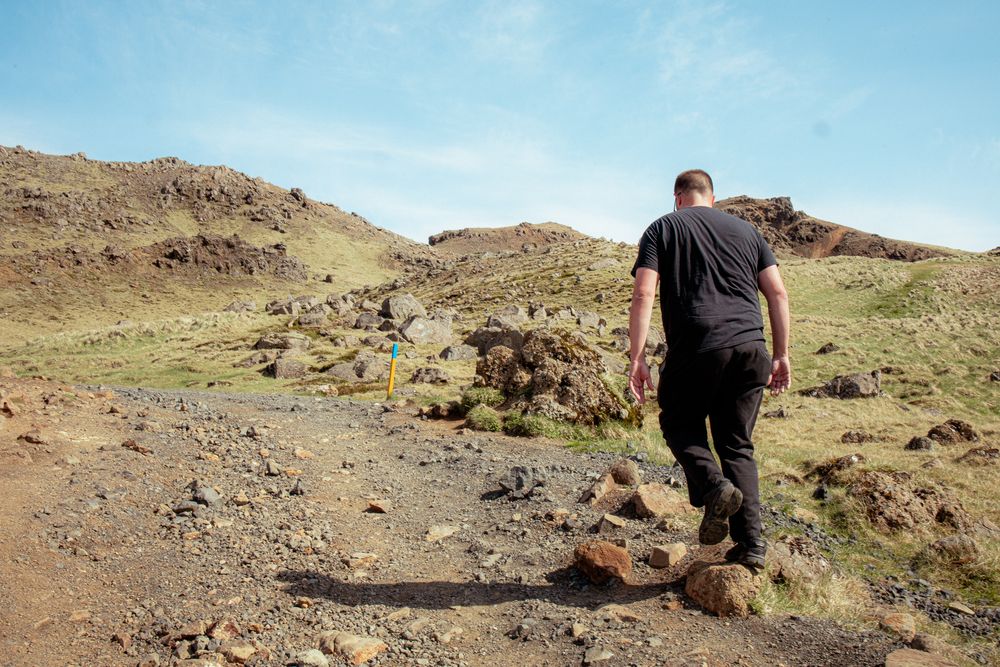 A hiker walks along a rocky trail through desert hills under blue sky.
