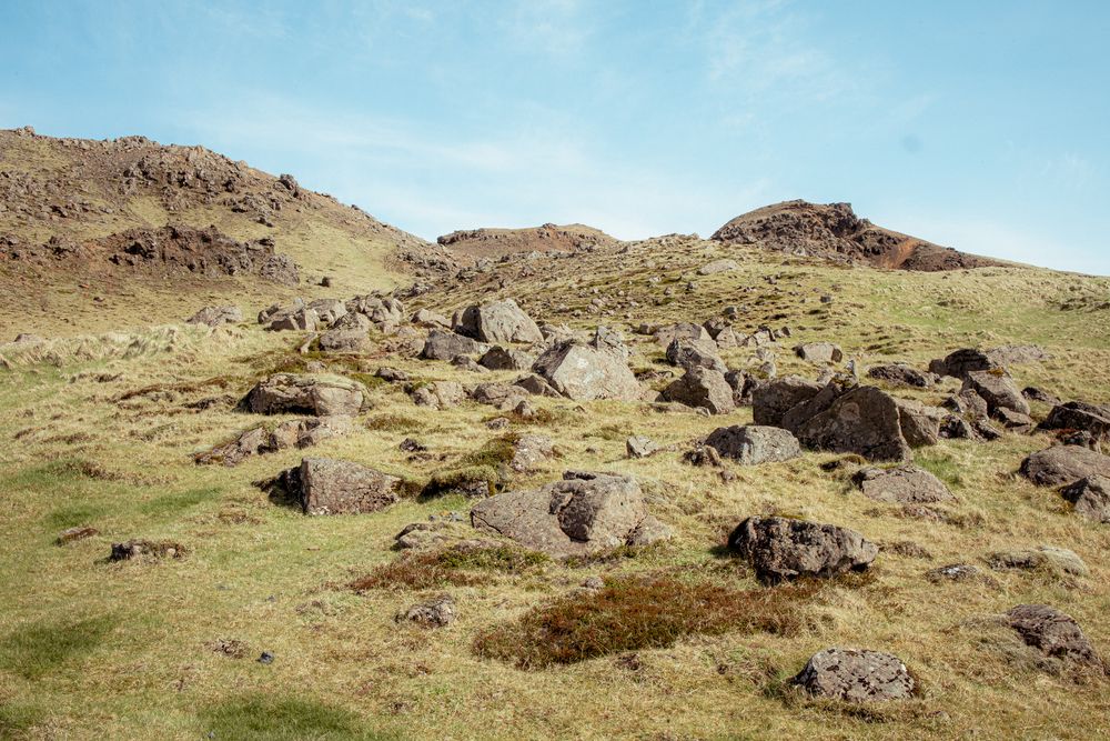 Rocky landscape with scattered boulders on grassy hillside under blue sky in arid terrain.
