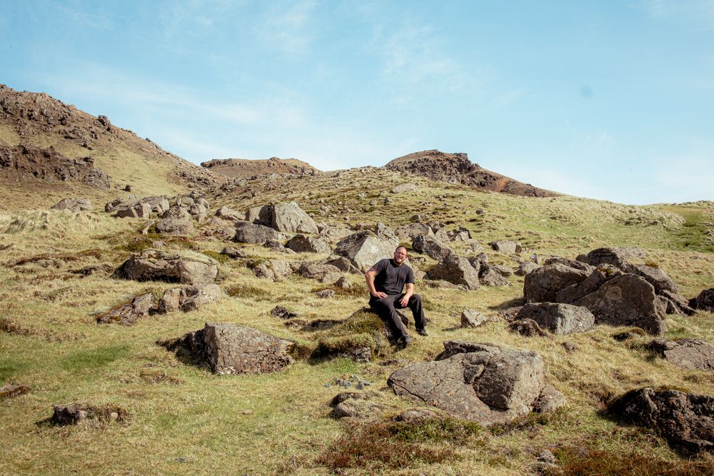 Rocky mountain slope with scattered boulders and grass patches under blue sky on a sunny day.
