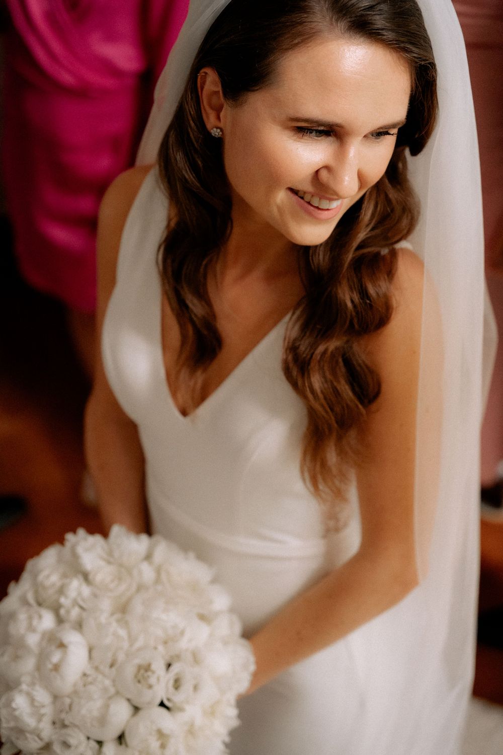A bride in a classic white wedding dress smiles while holding a white rose bouquet.