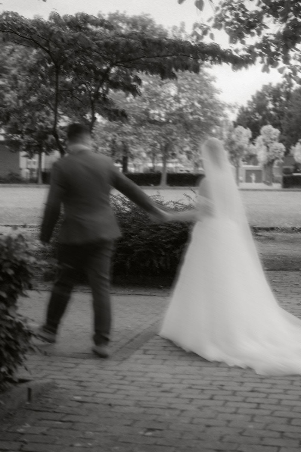 Black and white artistic photograph of a newlywed couple walking down a brick path during their outdoor wedding.