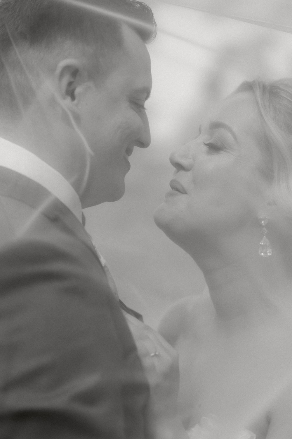 A romantic black and white wedding photograph showing a tender moment between a couple about to kiss.