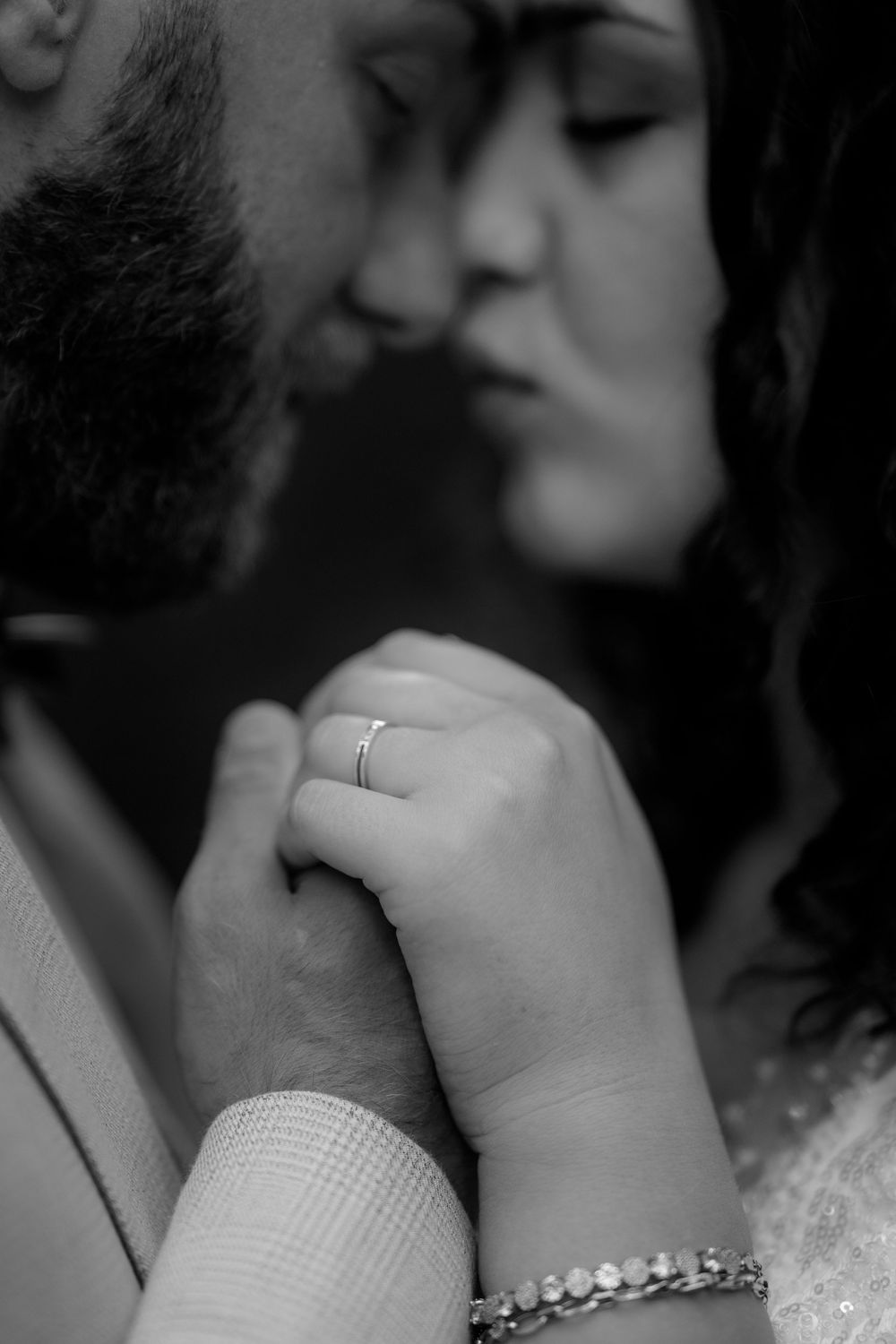 Black and white intimate close-up of an engaged couple's tender moment with a ring and bracelet visible.