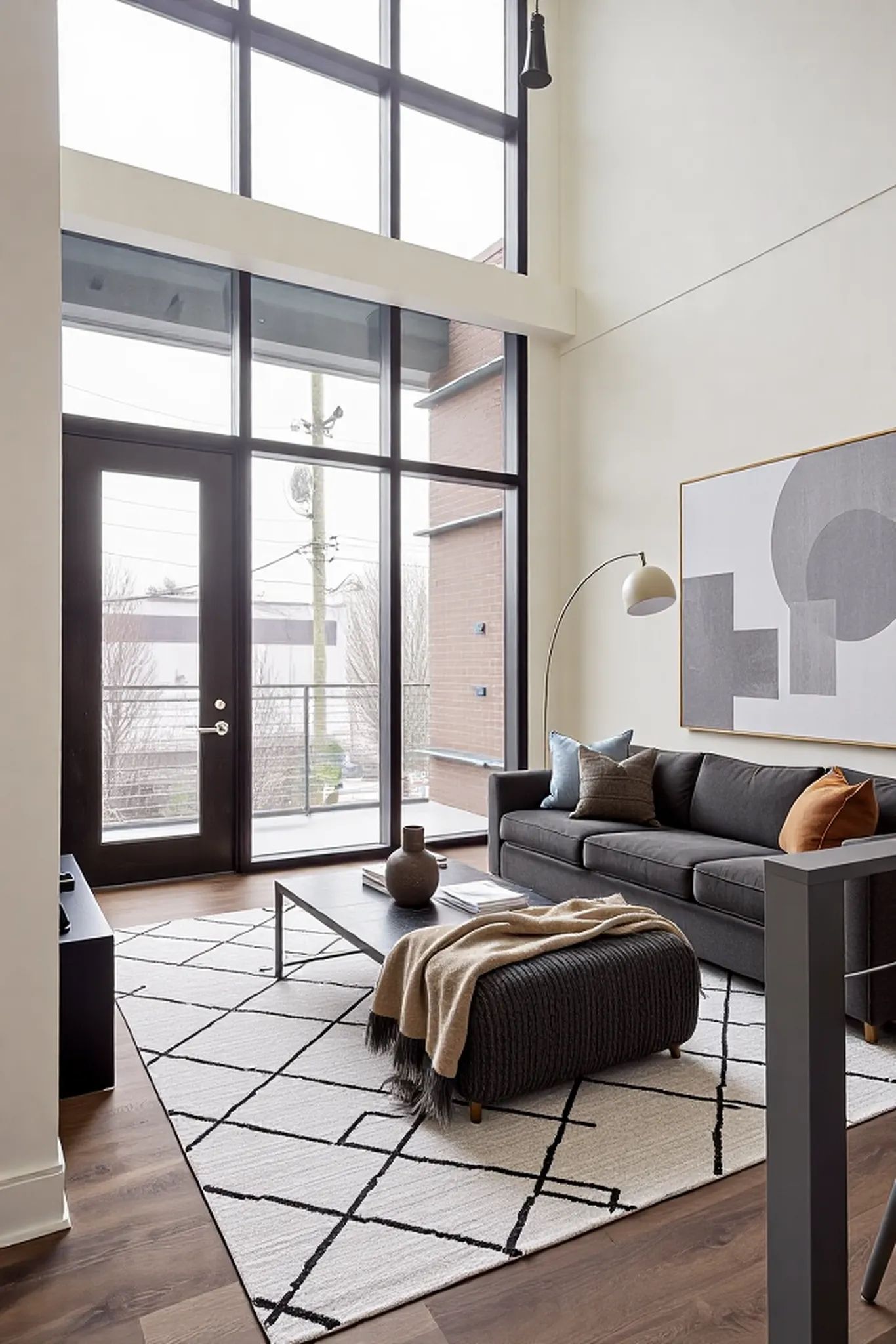 Virtually staged living room with floor-to-ceiling windows, modern black sofa, abstract art, and contemporary neutral decor.