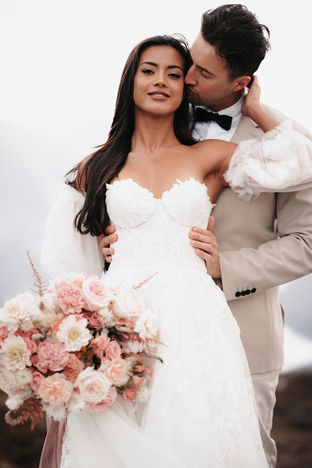 An intimate wedding photo captures a loving moment between newlyweds with a beautiful blush and white rose bouquet.