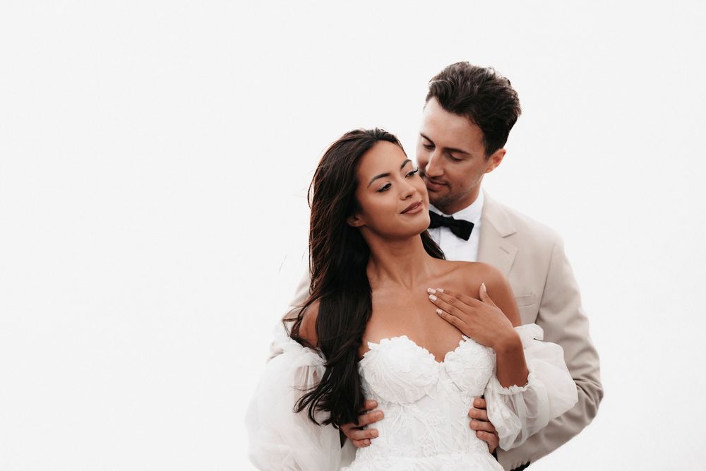 A romantic moment between newlyweds in wedding attire against a white background.