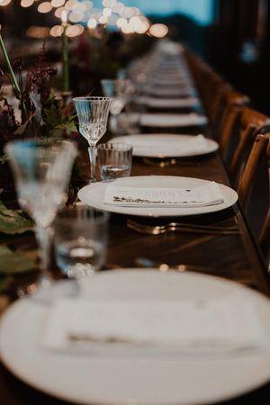 Elegant wedding reception table setting with white plates and crystal glasses arranged in a long row rustic table at The Astoria, Porto