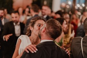 A couple share an intimate kiss on the dance floor during a wedding reception with guests in the background.
