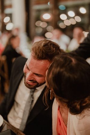 A couple laughing together at a wedding party with soft bokeh lights in the background.