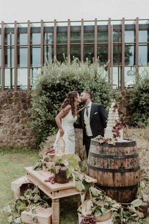 A romantic wedding scene with a rustic cake display featuring wooden barrels and floral decorations in an outdoor setting - The Astoria