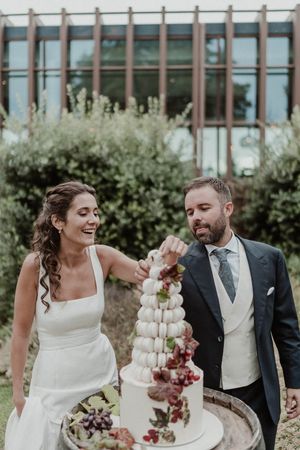 A couple shares a joyful moment while cutting their elegant multi-tiered white wedding cake decorated at The Astoria