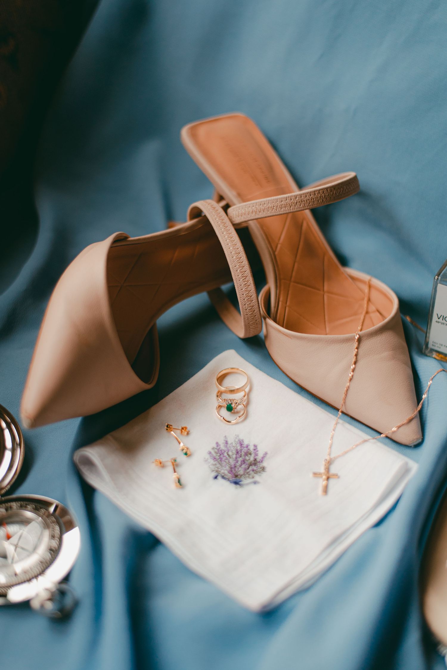 Flatlay shot of the bride's shoes, handkerchief, good rings, necklace, earrings on a blue backdrop