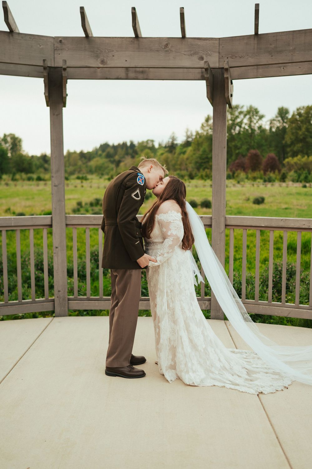 A romantic wedding moment captured under a wooden pergola in a garden setting with a long flowing white lace dress and veil.