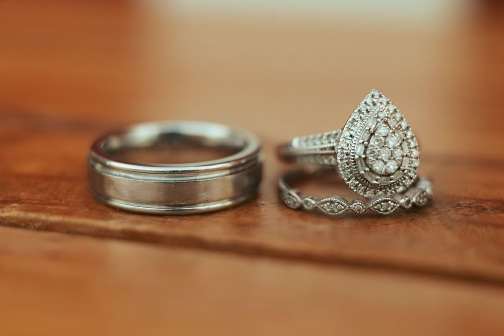 Wedding ring set featuring a vintage-style pear-shaped diamond engagement ring and classic men's wedding band on wooden surface.