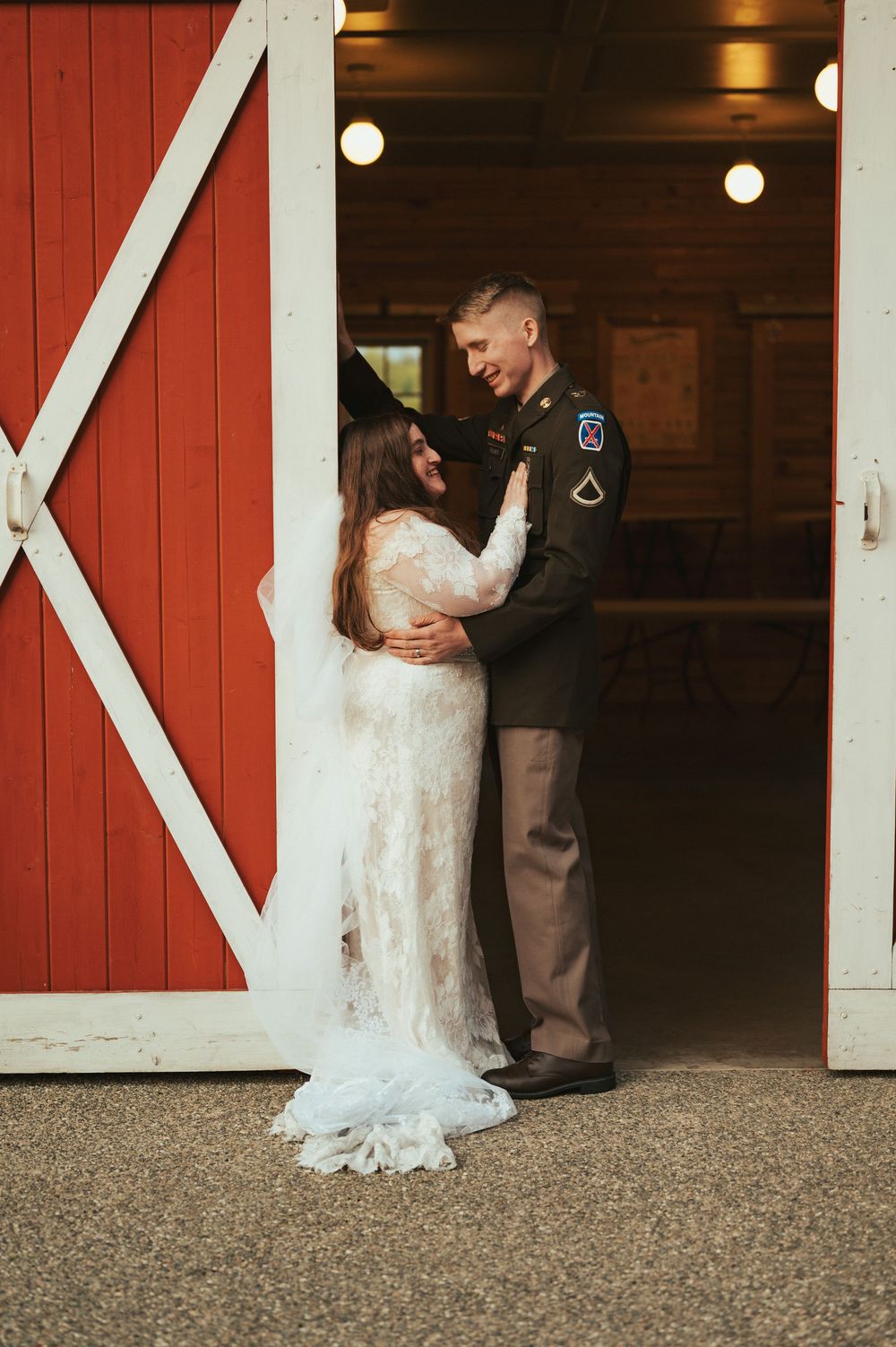 Newlywed couple embraces in doorway of red barn during rustic wedding photoshoot.