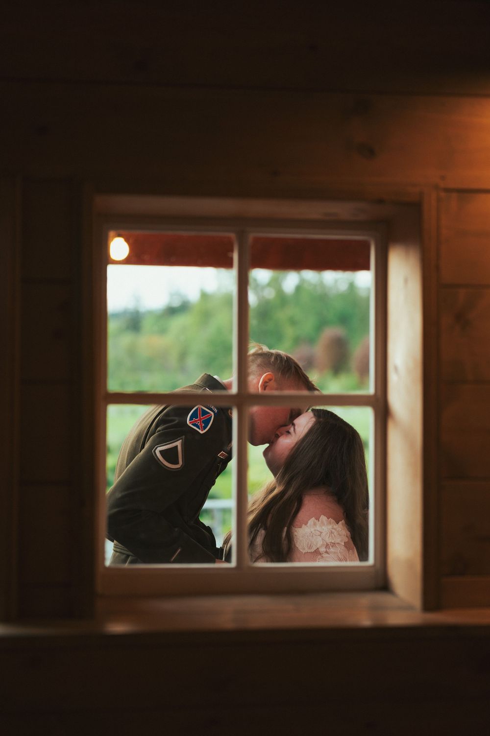 Romantic silhouette of a couple framed through a rustic window at sunset in an intimate moment.