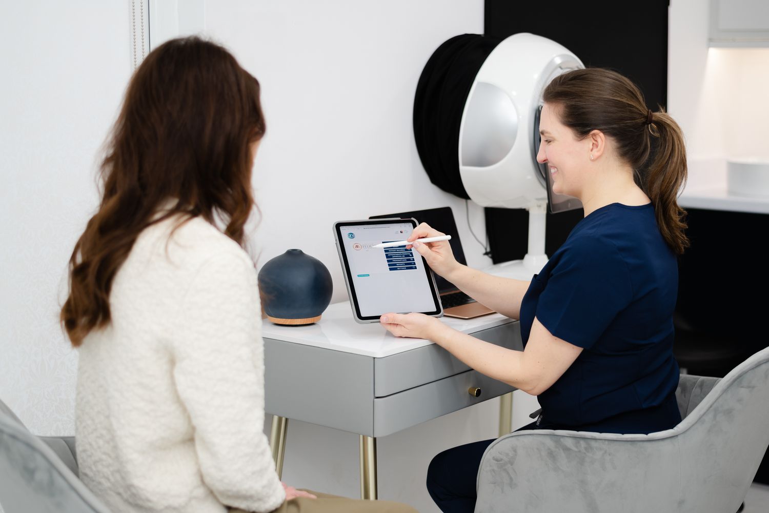 A medical consultation in progress with two people looking at a digital tablet in a clinical office setting.