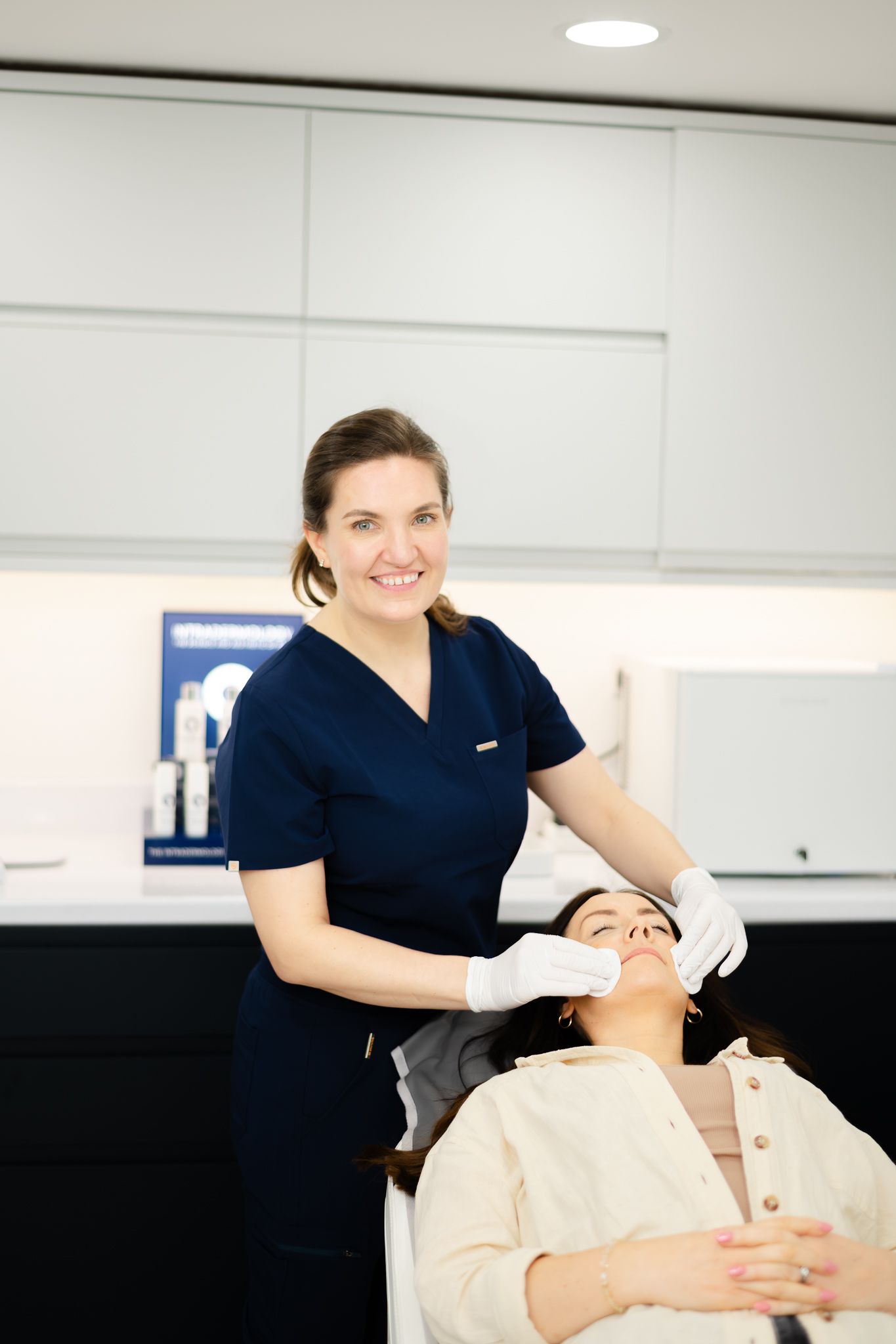 A dental professional in navy blue scrubs performs a procedure on a patient reclined in a treatment chair.