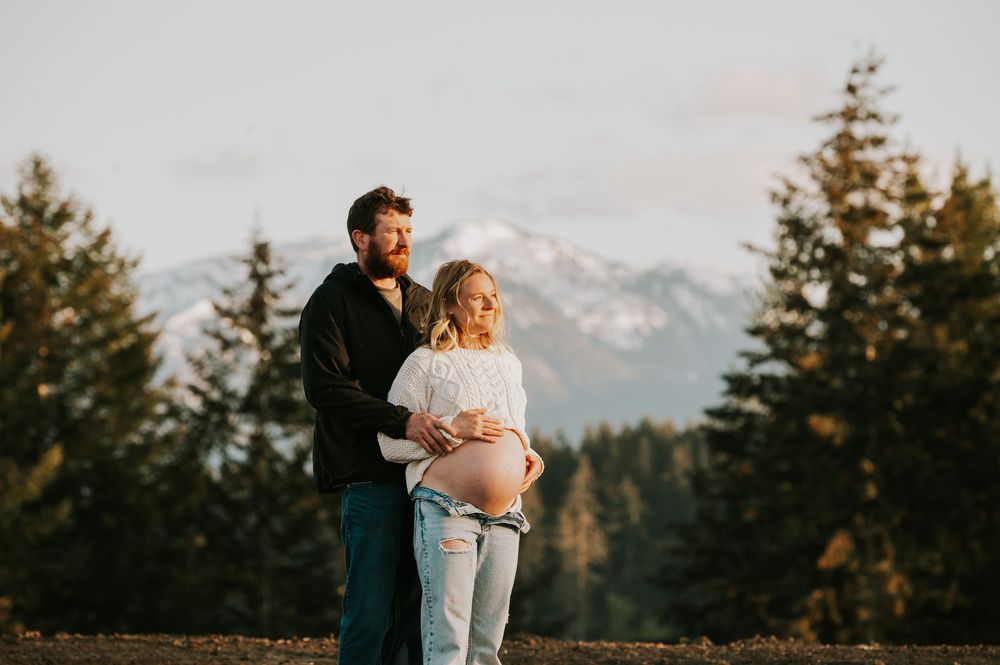 Maternity candid photography of couple holding belly in front of beautiful mountain views on Vancouver island golden hour light photographer
