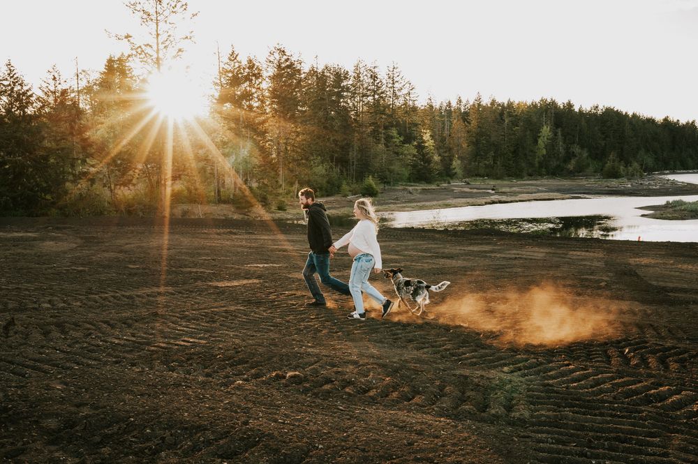 Maternity candid portrait couple running on hill close to ocean dusty golden hour light beams Vancouver Island natural feeling photographer