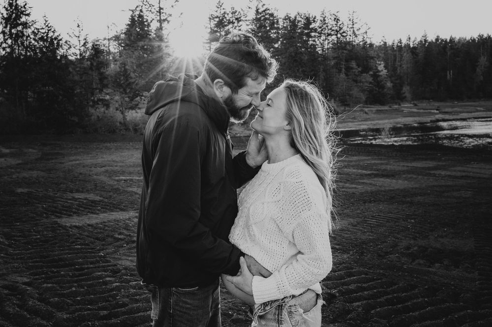 Maternity portrait of couple embracing on hill close to ocean dusty golden hour light beams Vancouver Island natural feeling photographer