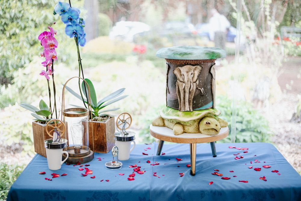 Blue tablecloth decorated table with pink and blue orchids, vintage decor items, and an ornate metallic elephant holder.