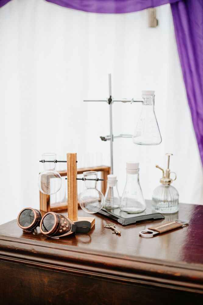 Vintage laboratory equipment setup with glass beakers, steampunk goggles and metal stands on a wooden table.