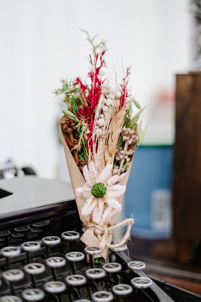 A vintage typewriter with a small bouquet of red and white dried flowers wrapped in paper resting on its keys.