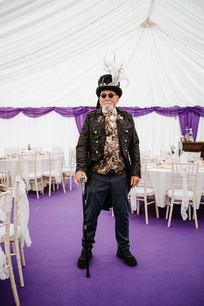 A steampunk-styled outfit featuring a black top hat and coat in an elegant white tent with purple decor.