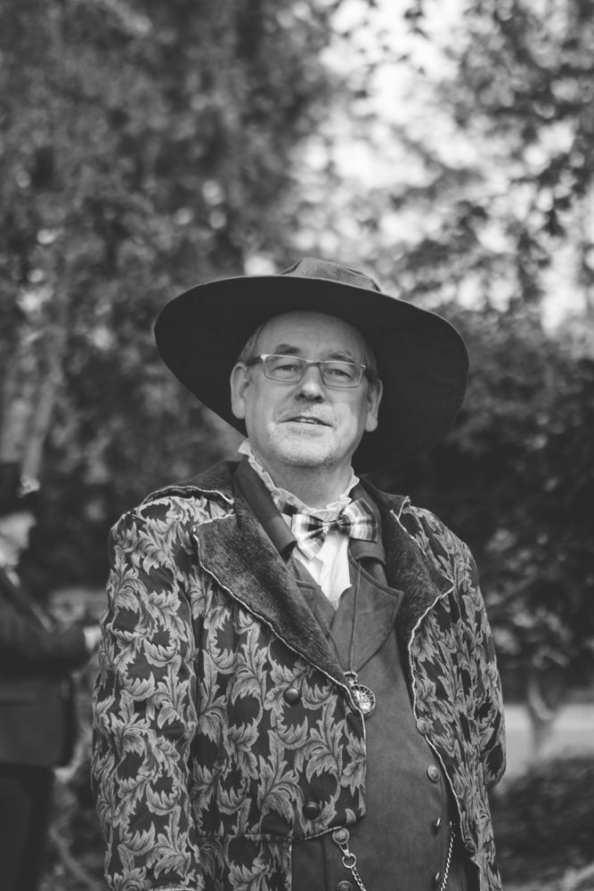 A black and white portrait of someone in vintage attire with a wide-brimmed hat and patterned jacket.
